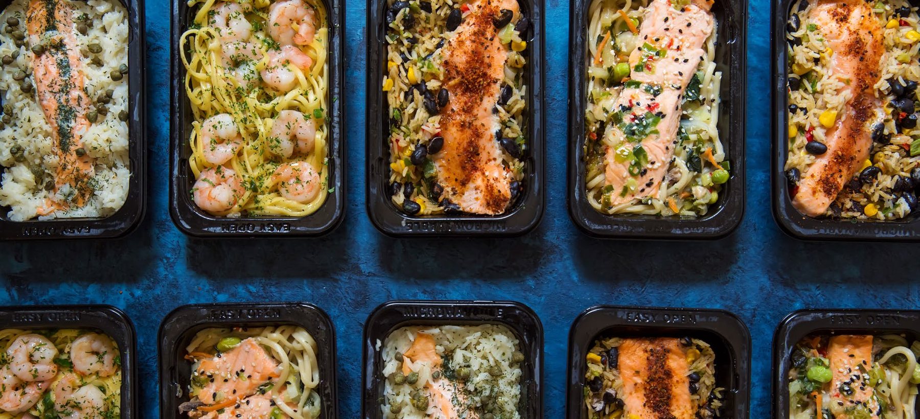 Composed meal trays with salmon, pasta, and bowls